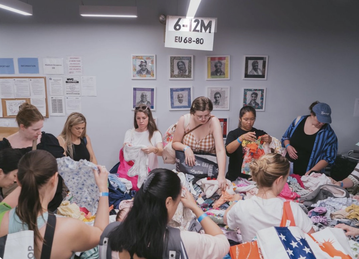 Women browsing tables of nearly-new baby clothes at a swap