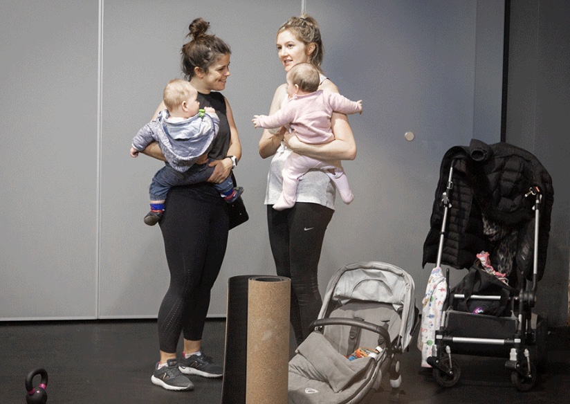 Two mums chatting and laughing together after class, each holding a baby