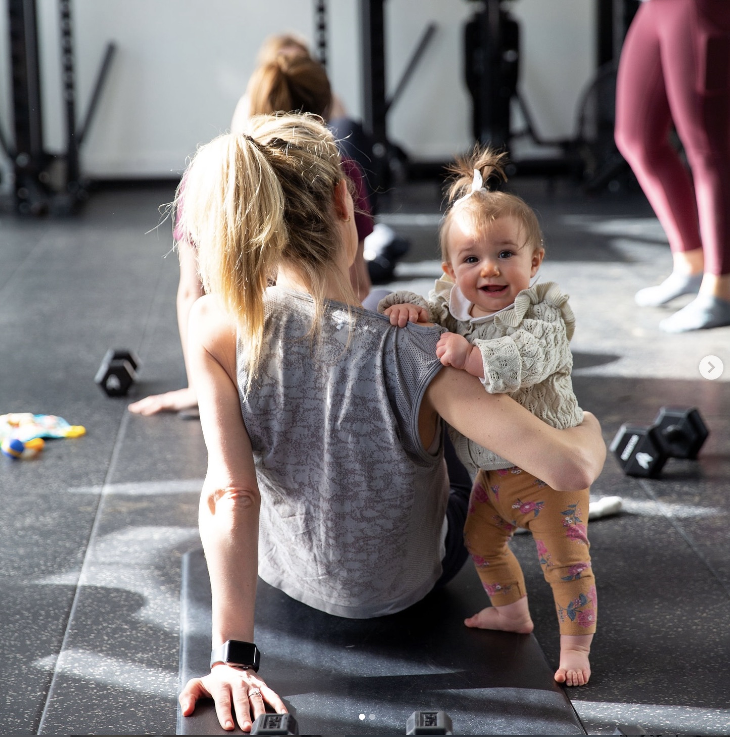 A mum doing strength work on the floor with her baby smiling beside her